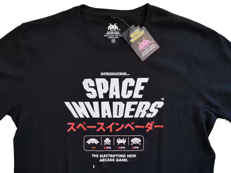 Black Space Invaders T-shirt styled like a vintage arcade advertisement, with bold headline text, Japanese lettering, and orderly pixel alien graphics.