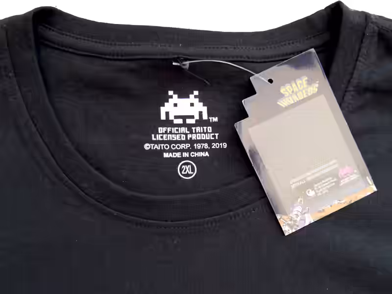 Close-up of the T-shirt collar showing the neck label and a Taito hologram authenticity tag confirming official Space Invaders licensing.