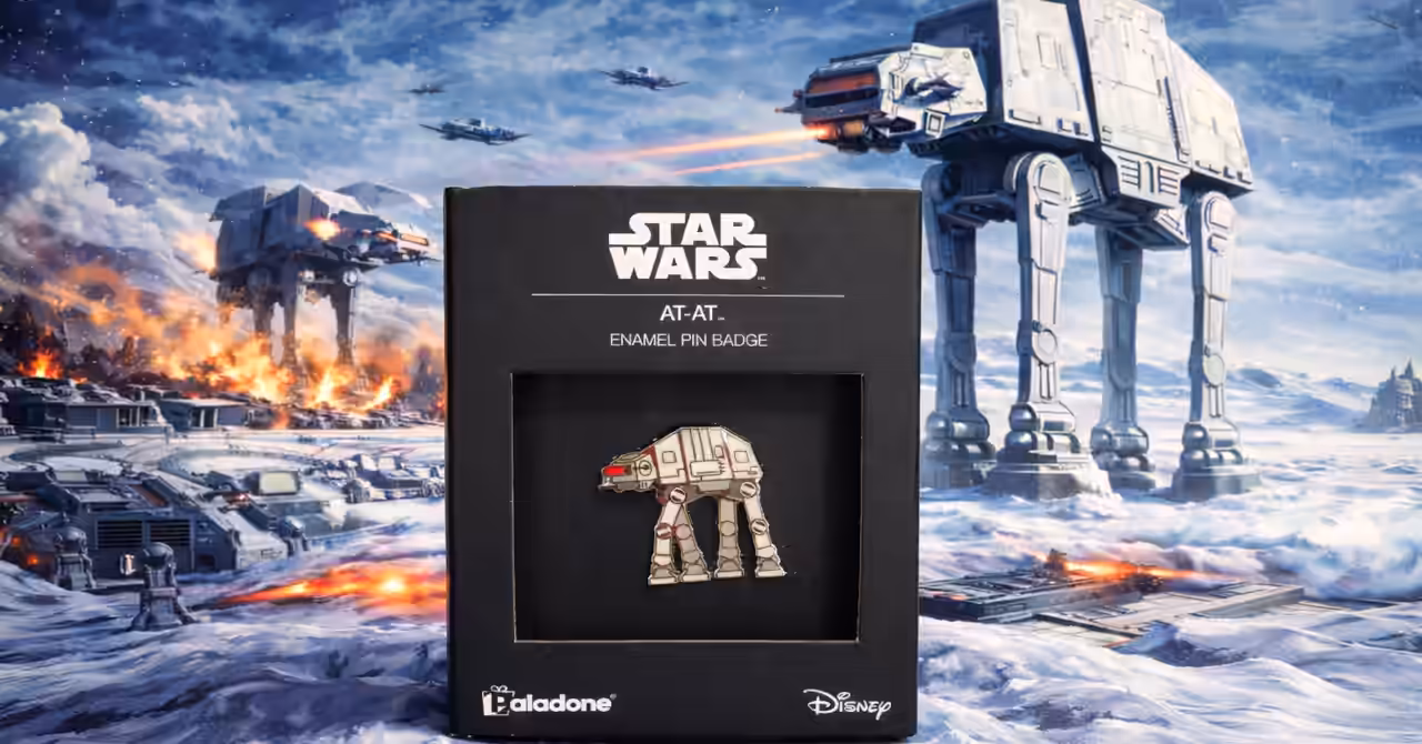 Star Wars AT-AT enamel pin in retail box over a snowy sci-fi battle scene with AT-AT walkers advancing on a rebel base