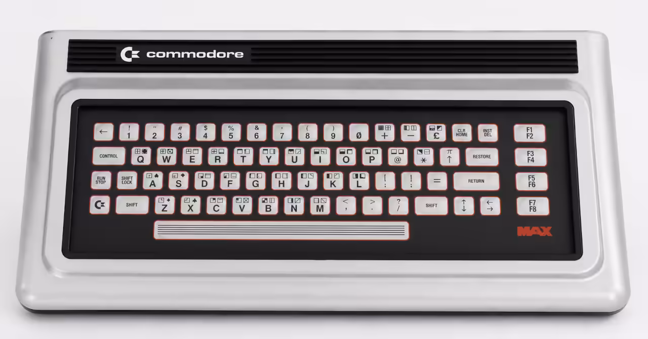 Studio-style gallery image of a Commodore MAX Machine showing its silver case, black membrane keyboard panel, Commodore badge and red MAX logo.