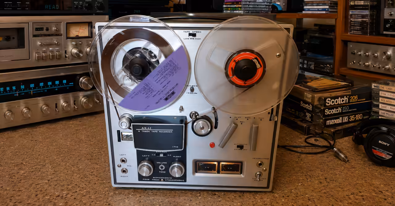 AKAI 1710W reel-to-reel tape recorder surrounded by vintage hi-fi components, open reels and classic audio gear in a collector's listening room.